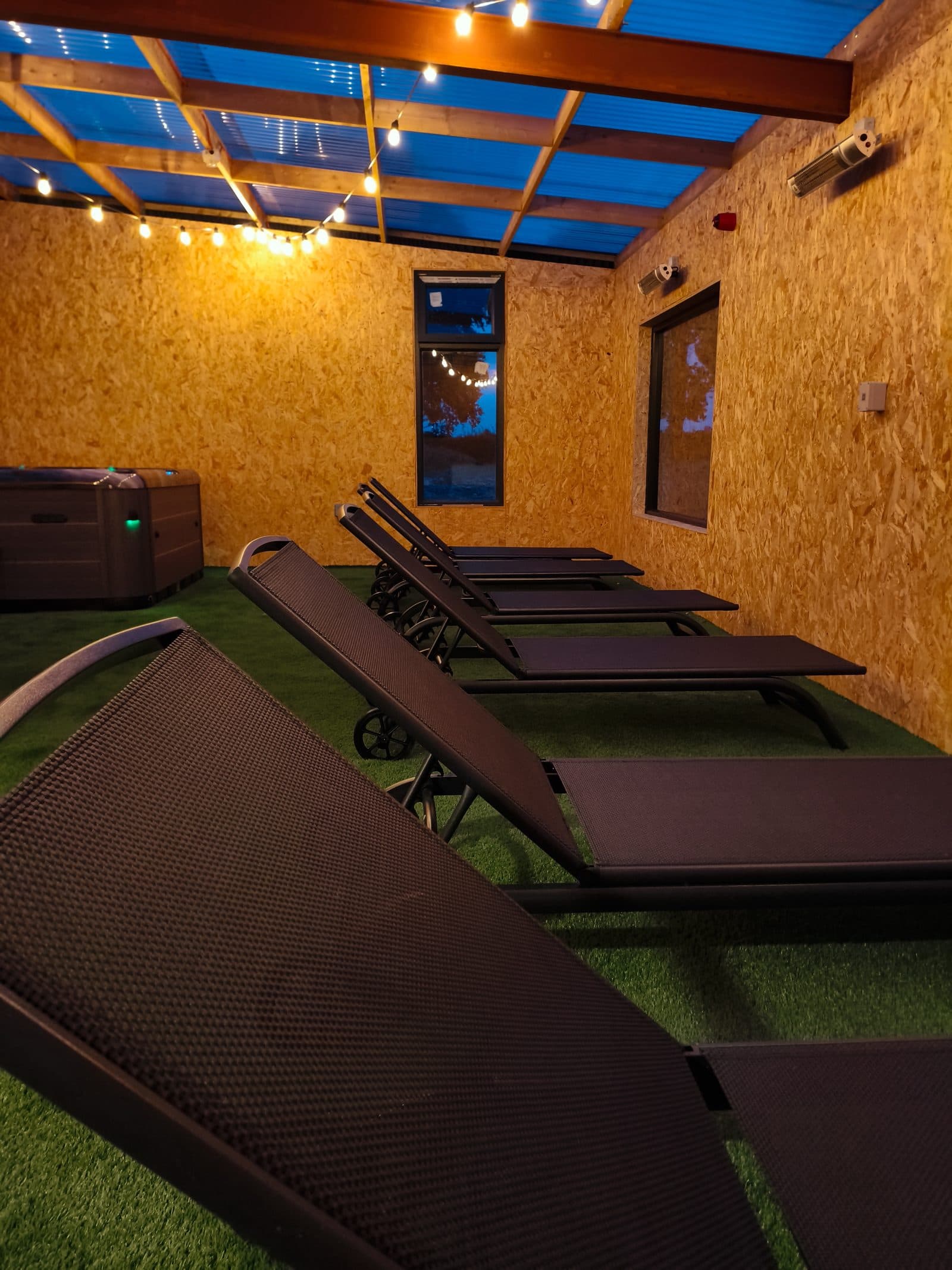 Loungers on the covered deck at dusk, hot tub and string lights